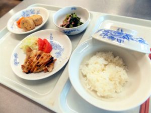 介護施設の食事風景。ご飯、焼き魚、野菜、惣菜などの配膳。